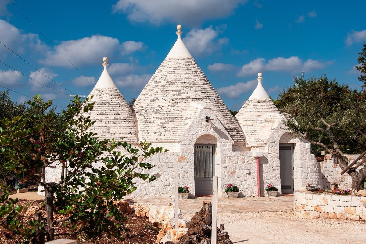 Il trullo LiberaMente: i coni in pietra sotto il cielo azzurro e, davanti, la porta d’ingresso