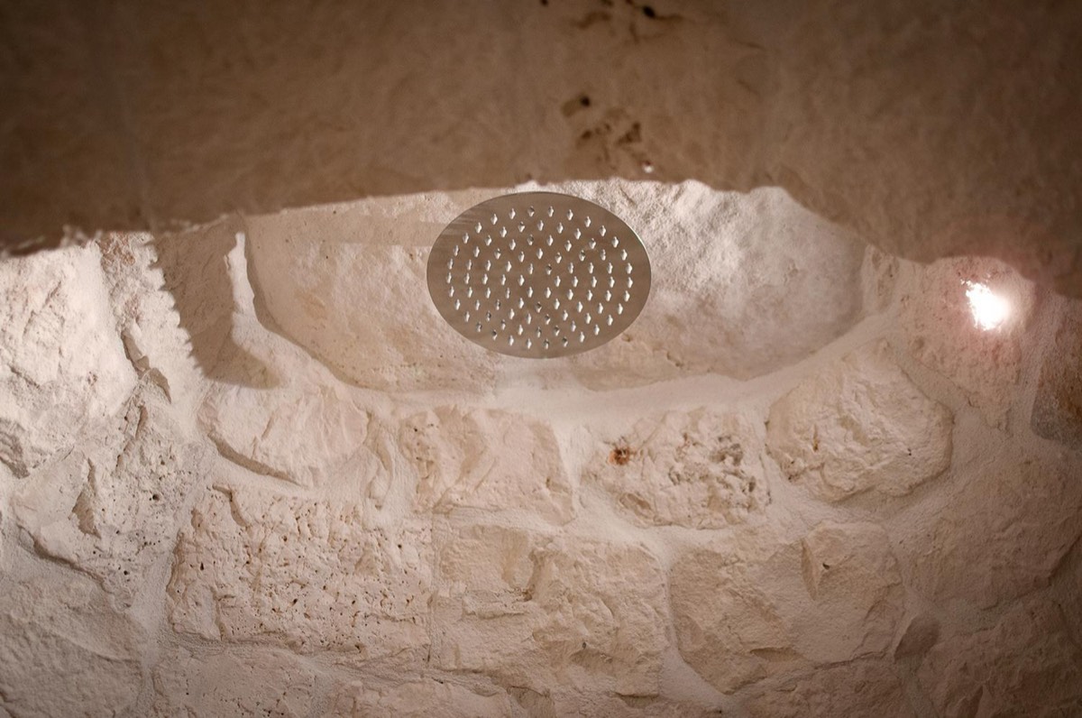 Il soffione rotondo della doccia, appeso dentro il cono di pietra
